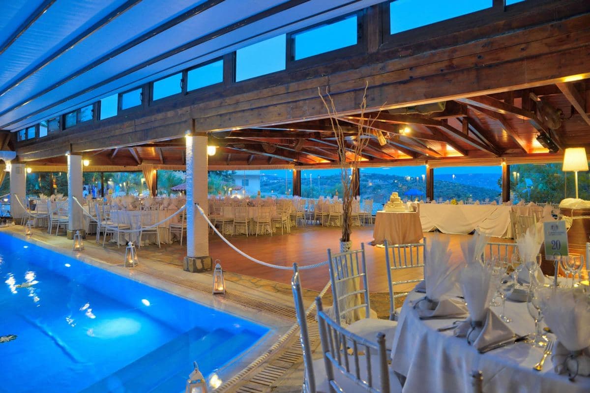 Αίθουσα δεξιώσεων με στρωμένα τραπέζια και πισίνα στο λυκόφως — κτήμα γάμου Φιλόκαλις Κορωπί