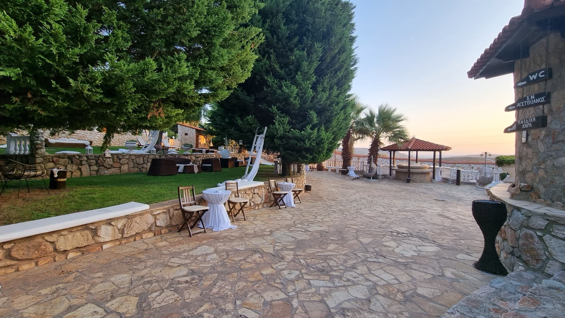 Πράσινοι εξωτερικοί χώροι με γκαζόν και πέτρινο γεφυράκι στο κτήμα δεξιώσεων Αττική